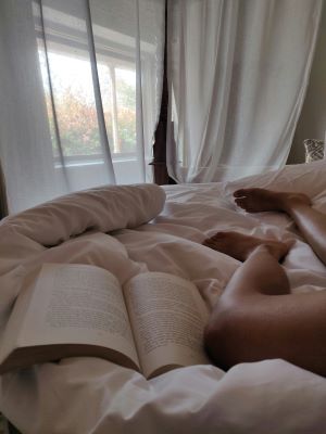 A persons legs on a bed beside a book